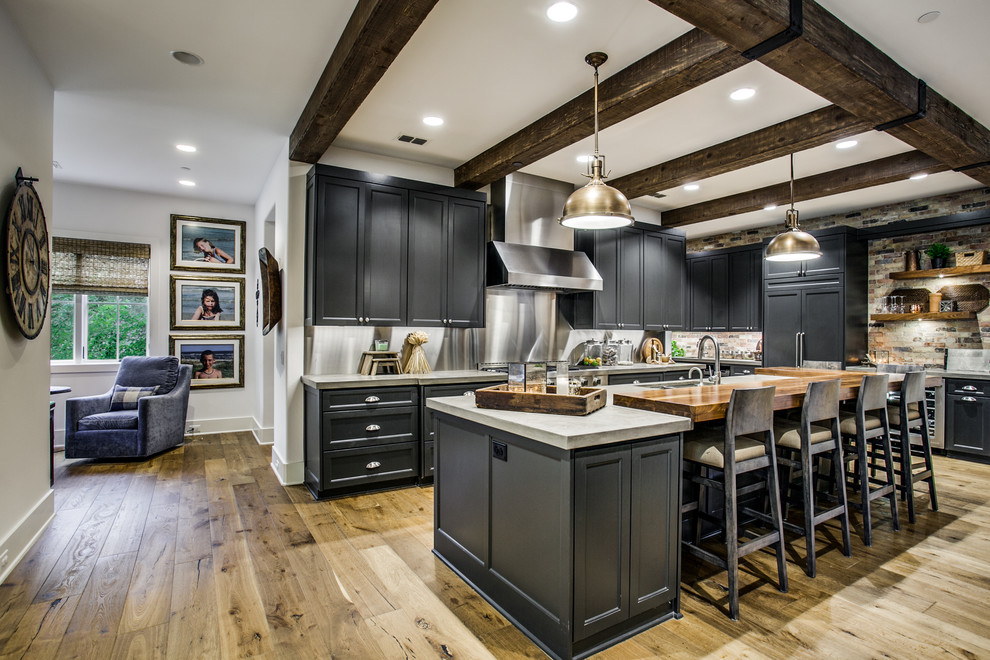 Transitional l-shaped kitchen in Dallas with an undermount sink, recessed-panel cabinets, black cabinets, grey splashback, light hardwood floors, with island, brown floor and grey benchtop.