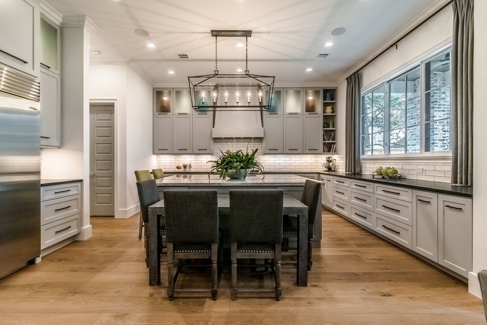This is an example of a large transitional kitchen in Houston with shaker cabinets, grey cabinets, quartzite benchtops, white splashback, subway tile splashback, stainless steel appliances, light hardwood floors and multiple islands.