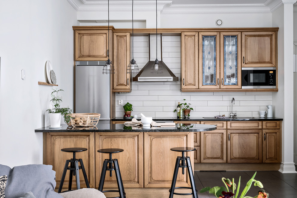 Design ideas for a mid-sized transitional single-wall open plan kitchen in Gothenburg with medium wood cabinets, granite benchtops, stainless steel appliances, a peninsula, black floor, raised-panel cabinets and grey splashback.