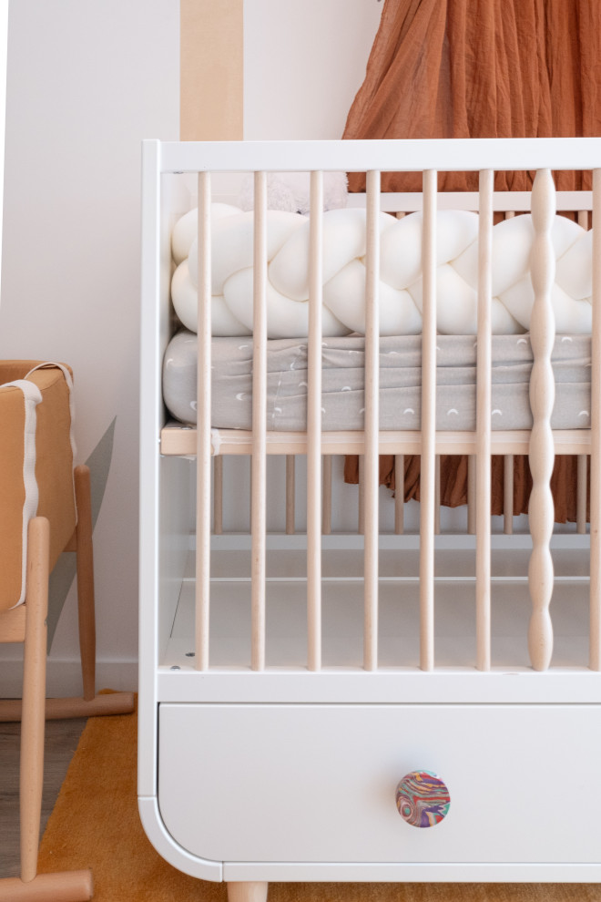 Modelo de habitación de bebé neutra contemporánea pequeña con parades naranjas, suelo de madera clara, suelo beige, papel pintado y papel pintado