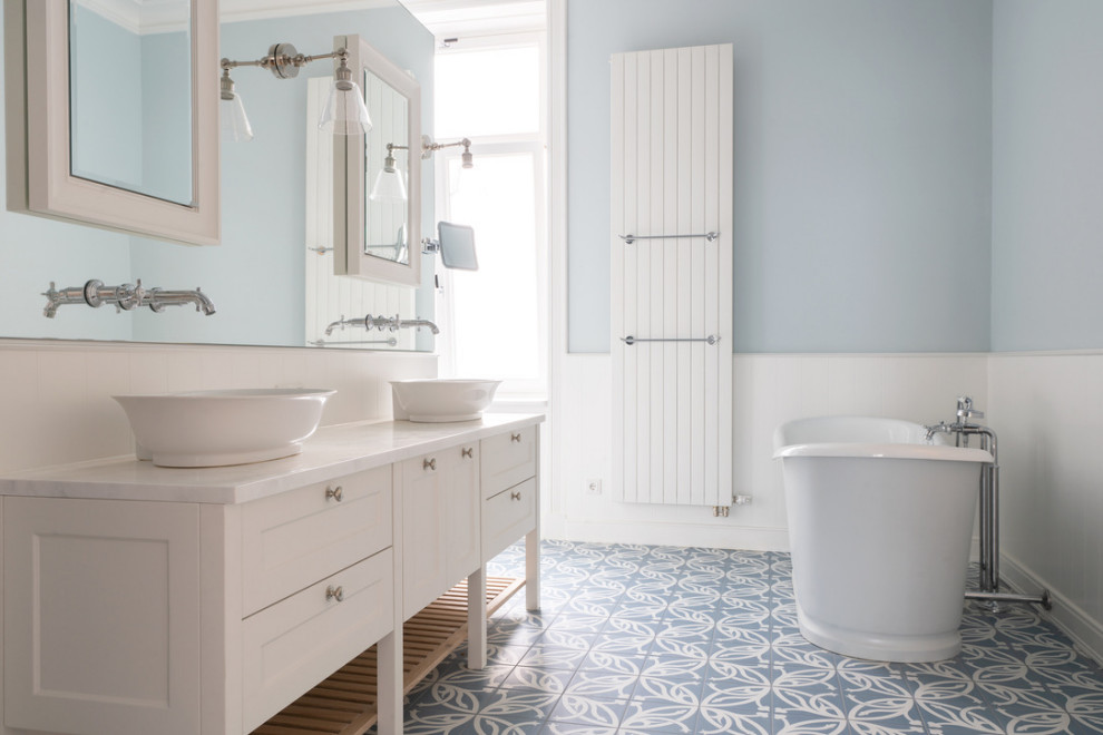 Photo of a large country master bathroom in Hamburg with shaker cabinets, white cabinets, a freestanding tub, a wall-mount toilet, white tile, blue walls, ceramic floors, wood benchtops, blue floor, an open shower, white benchtops, an enclosed toilet, a double vanity, a freestanding vanity and panelled walls.