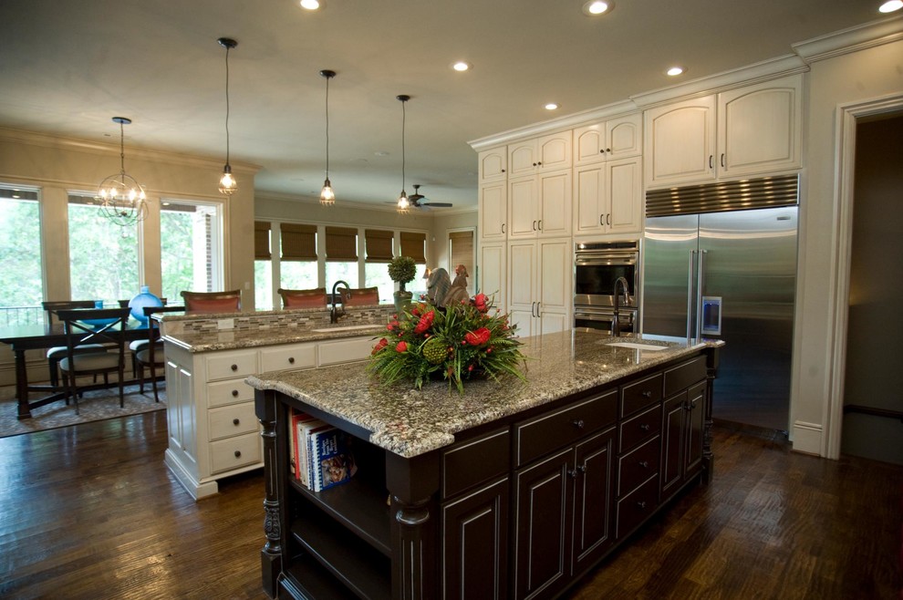 Huge l-shaped medium tone wood floor eat-in kitchen photo with an undermount sink, raised-panel cabinets, white cabinets, granite countertops, beige backsplash, matchstick tile backsplash, stainless steel appliances and two islands