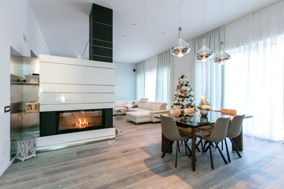 Inspiration for a large contemporary dining room in Bologna with white walls, dark hardwood floors, a two-sided fireplace, a plaster fireplace surround and grey floor.