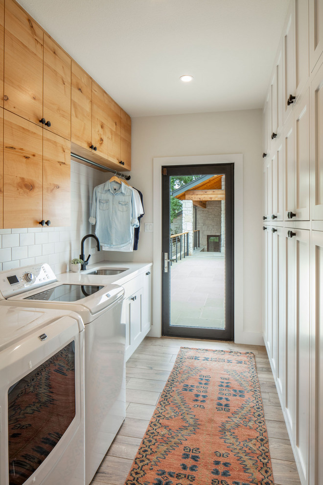 Photo of a country dedicated laundry room in Austin with an undermount sink, flat-panel cabinets, medium wood cabinets, white walls and a side-by-side washer and dryer.