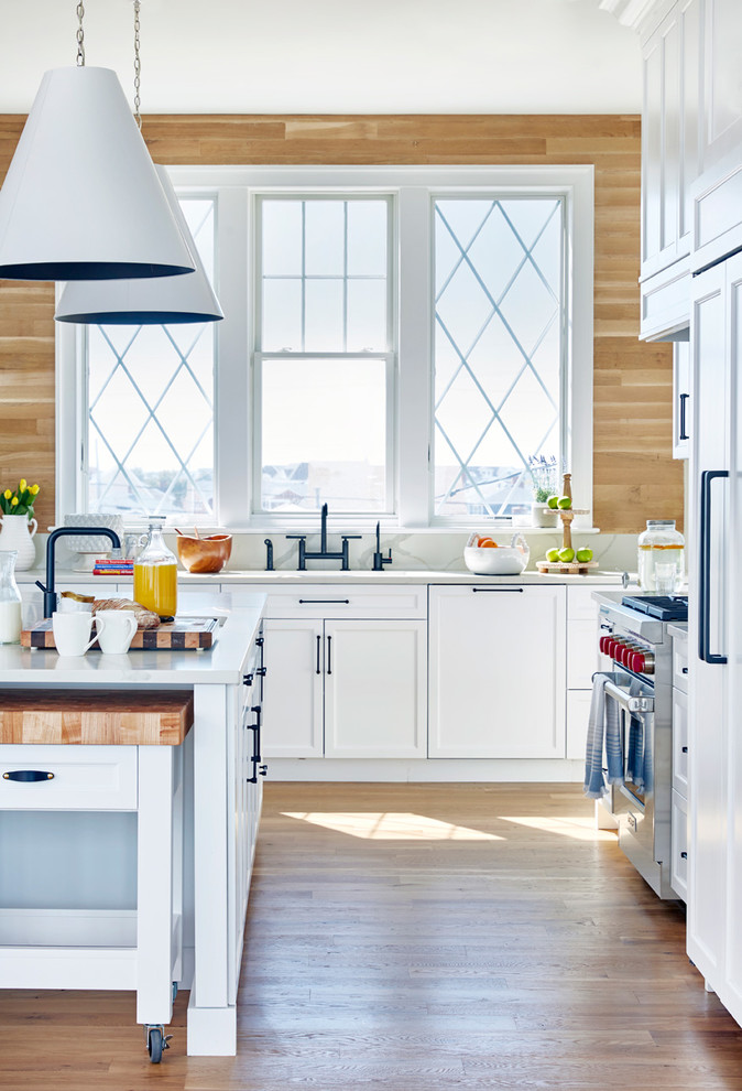Kitchen - coastal l-shaped medium tone wood floor and brown floor kitchen idea in New York with an integrated sink, shaker cabinets, white cabinets, brown backsplash, wood backsplash, stainless steel appliances, an island and white countertops
