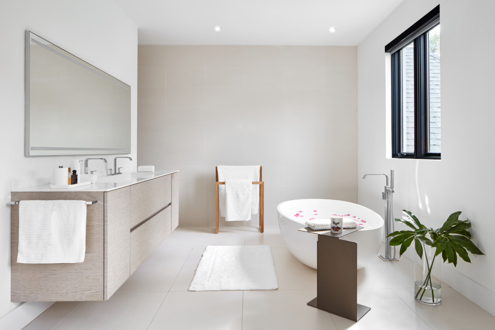 Inspiration for a contemporary master bathroom in Toronto with flat-panel cabinets, light wood cabinets, a freestanding tub, beige walls, an integrated sink, beige floor and white benchtops.