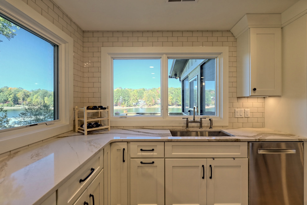 Design ideas for a mid-sized country l-shaped open plan kitchen in Atlanta with an undermount sink, shaker cabinets, white cabinets, quartz benchtops, white splashback, subway tile splashback, stainless steel appliances, laminate floors, with island, brown floor and white benchtop.