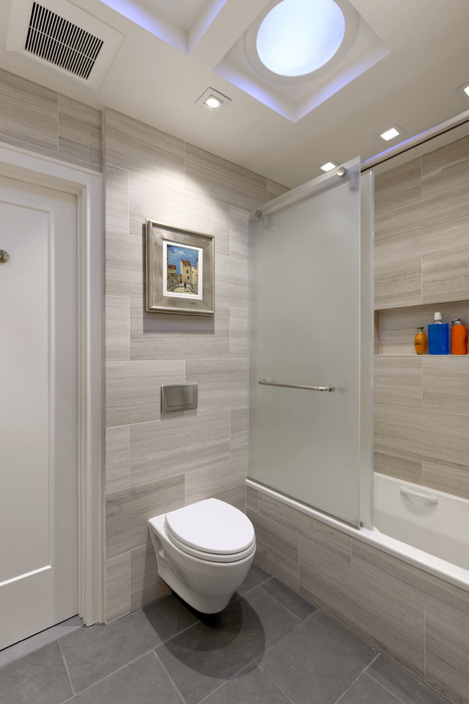 Design ideas for a mid-sized contemporary kids bathroom in DC Metro with furniture-like cabinets, medium wood cabinets, an alcove tub, a shower/bathtub combo, a wall-mount toilet, gray tile, marble, grey walls, slate floors, a vessel sink, limestone benchtops, black floor, a sliding shower screen and grey benchtops.