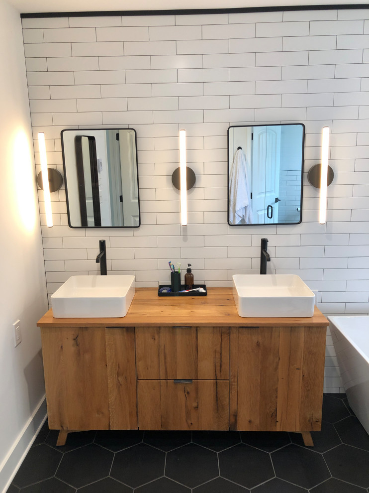 Inspiration for a mid-sized modern master bathroom in Philadelphia with flat-panel cabinets, distressed cabinets, a freestanding tub, a corner shower, white tile, white walls, a pedestal sink, wood benchtops, black floor, a hinged shower door, brown benchtops, a double vanity and a freestanding vanity.