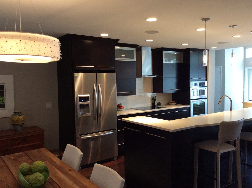 Inspiration for a large transitional galley eat-in kitchen remodel in Chicago with an undermount sink, flat-panel cabinets, black cabinets, solid surface countertops, white backsplash, glass tile backsplash, stainless steel appliances and an island