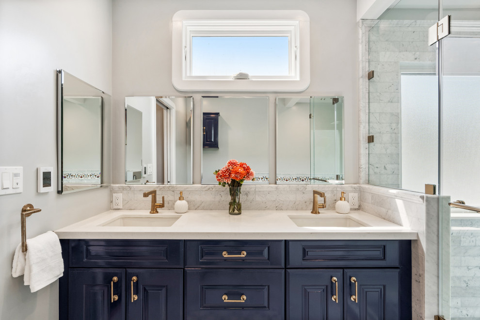 Источник вдохновения для домашнего уюта: большая главная, серо-белая ванная комната в стиле неоклассика (современная классика) с фасадами с выступающей филенкой, синими фасадами, отдельно стоящей ванной, угловым душем, биде, серой плиткой, мраморной плиткой, серыми стенами, мраморным полом, врезной раковиной, столешницей из искусственного кварца, серым полом, душем с распашными дверями, белой столешницей, тумбой под две раковины и встроенной тумбой