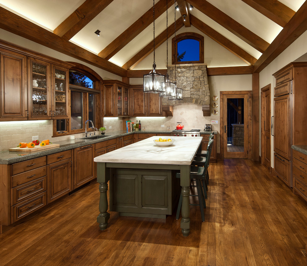 Inspiration for a country u-shaped kitchen in Denver with an undermount sink, raised-panel cabinets, dark wood cabinets, beige splashback, stone tile splashback, stainless steel appliances, dark hardwood floors and with island.