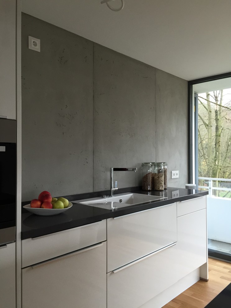 This is an example of a large contemporary single-wall open plan kitchen in Cologne with a drop-in sink, flat-panel cabinets, white cabinets, granite benchtops, grey splashback, cement tile splashback, stainless steel appliances, painted wood floors, no island and brown floor.