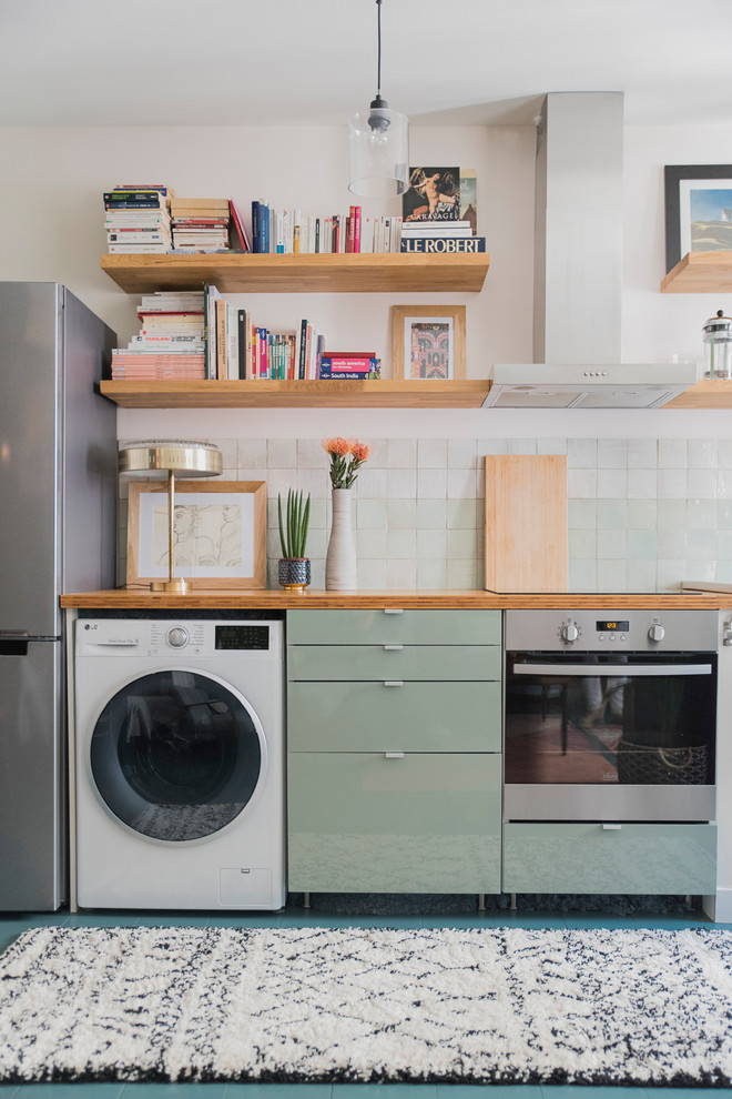 This is an example of a mid-sized transitional single-wall open plan kitchen in Paris with a drop-in sink, flat-panel cabinets, green cabinets, wood benchtops, green splashback, ceramic splashback, painted wood floors and blue floor.