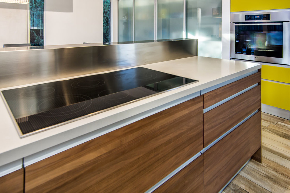 Small modern galley eat-in kitchen in San Francisco with a single-bowl sink, flat-panel cabinets, stainless steel cabinets, solid surface benchtops, metallic splashback, stone tile splashback, black appliances and porcelain floors.