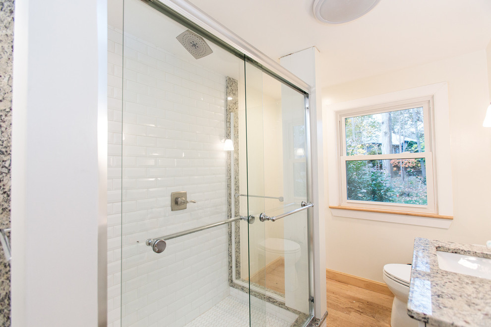 This is an example of a mid-sized transitional master bathroom in Boston with a corner shower, a two-piece toilet, white tile, beige walls, medium hardwood floors, a drop-in sink, granite benchtops and a sliding shower screen.