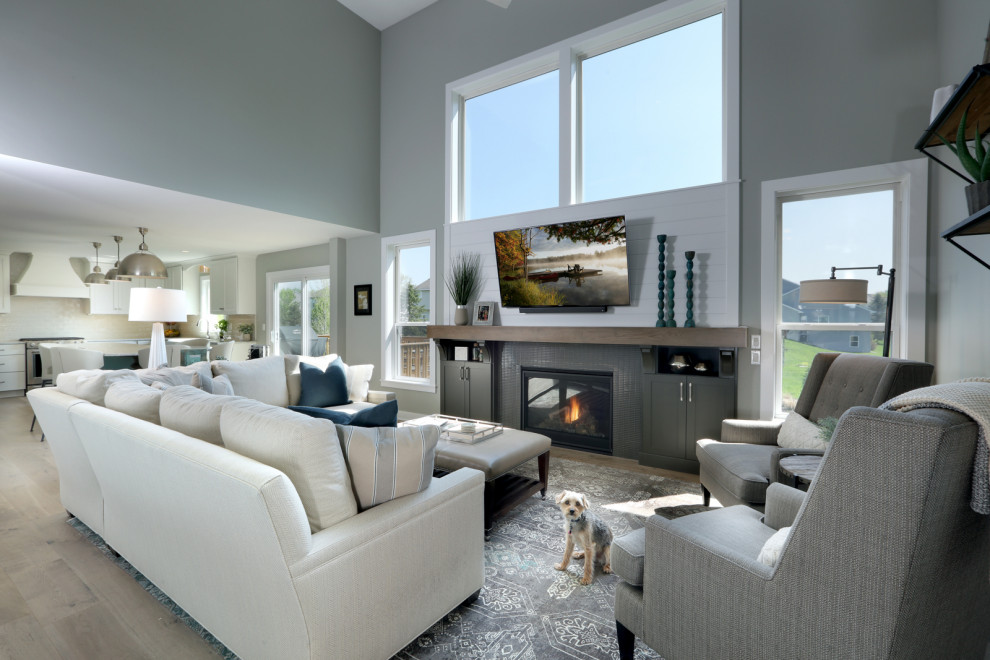 This is an example of a large traditional open concept living room in Grand Rapids with grey walls, light hardwood floors, a standard fireplace, a tile fireplace surround, a wall-mounted tv and vaulted.