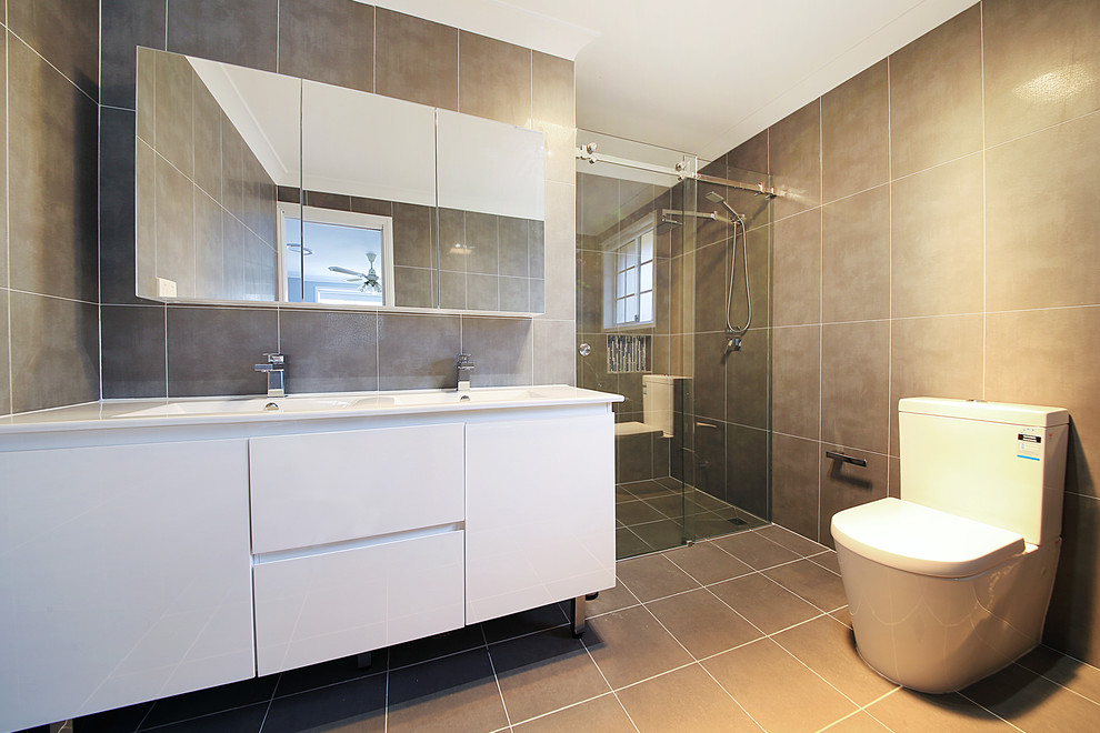 Inspiration for a large contemporary master bathroom in Sydney with a two-piece toilet, flat-panel cabinets, white cabinets, a freestanding tub, a corner shower, brown tile, cement tile, brown walls, an integrated sink, brown floor and a hinged shower door.
