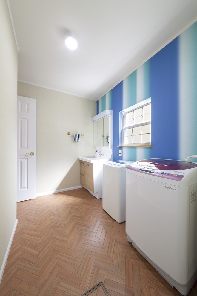 Photo of a beach style laundry room in Other with an integrated sink, multi-coloured walls, light hardwood floors, a side-by-side washer and dryer and brown floor.