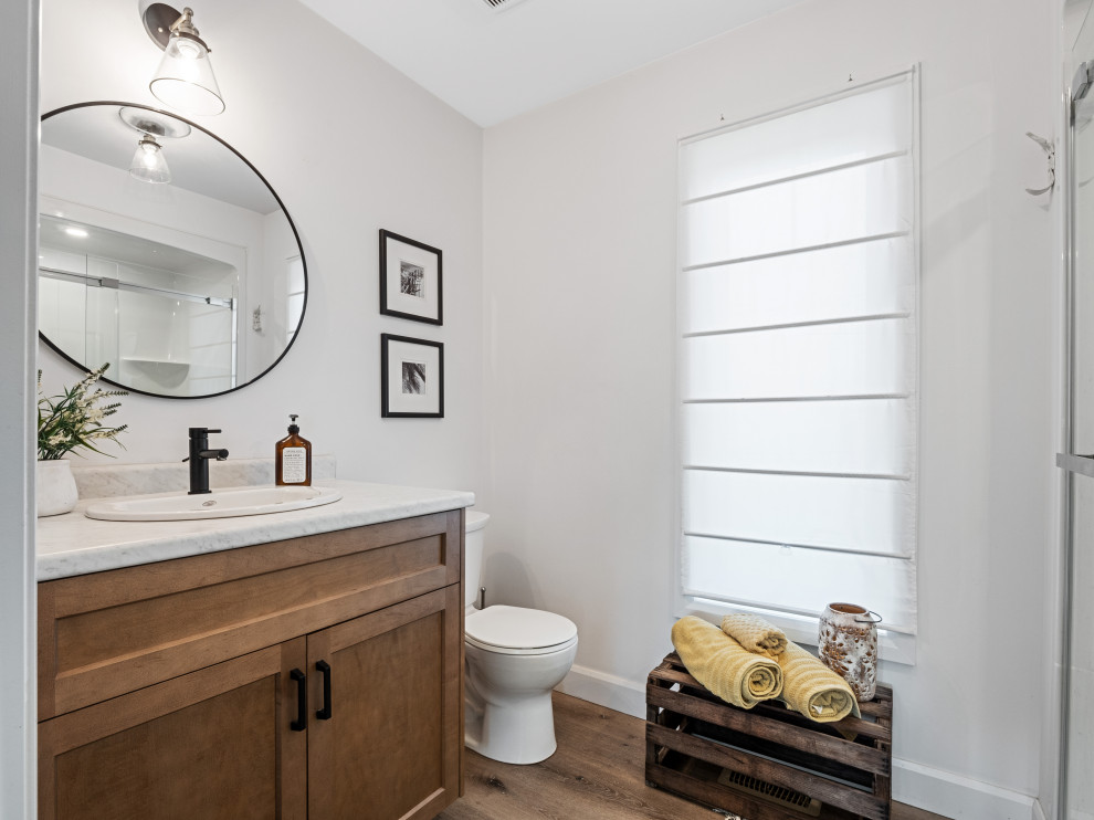 Modelo de cuarto de baño principal rústico pequeño con armarios con paneles empotrados, puertas de armario de madera oscura, sanitario de una pieza, paredes blancas y lavabo encastrado