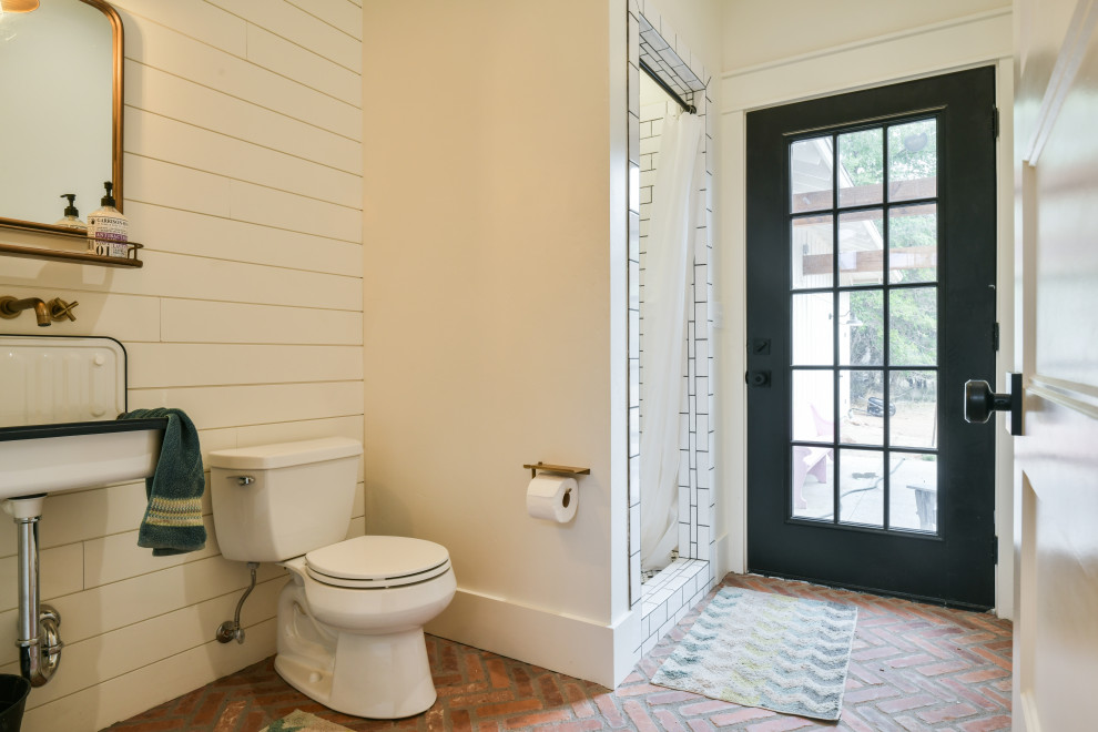 Bild på ett mycket stort amerikanskt badrum, med en dusch i en alkov, en toalettstol med hel cisternkåpa, vit kakel, keramikplattor, vita väggar, tegelgolv, ett fristående handfat, brunt golv och dusch med duschdraperi