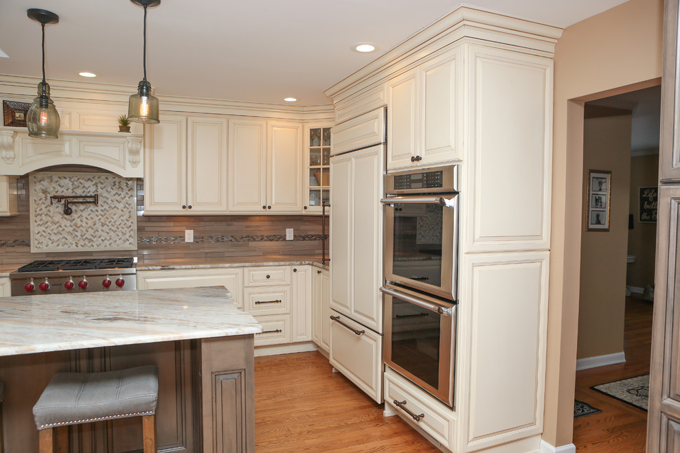Eat-in kitchen - large transitional u-shaped light wood floor eat-in kitchen idea in Newark with an undermount sink, raised-panel cabinets, distressed cabinets, granite countertops, brown backsplash, mosaic tile backsplash, stainless steel appliances and an island