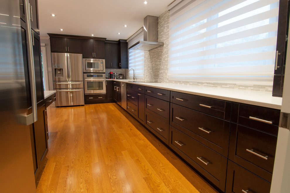 Inspiration for a large transitional galley light wood floor enclosed kitchen remodel in Toronto with a single-bowl sink, shaker cabinets, dark wood cabinets, quartzite countertops, beige backsplash, stone tile backsplash, stainless steel appliances and an island