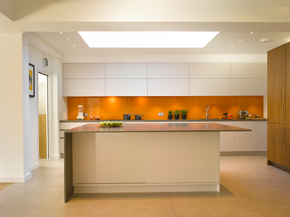 This is an example of a large contemporary single-wall open plan kitchen in London with flat-panel cabinets, white cabinets, quartzite benchtops, orange splashback, glass sheet splashback, panelled appliances, ceramic floors, with island, beige floor and beige benchtop.