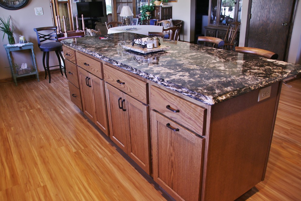 Example of a mid-sized l-shaped eat-in kitchen design with flat-panel cabinets, medium tone wood cabinets, quartz countertops, beige backsplash, black appliances and an island