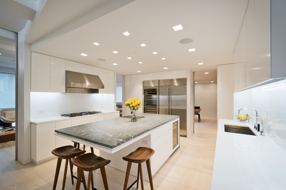 Design ideas for a modern u-shaped separate kitchen in New York with an undermount sink, flat-panel cabinets, white cabinets, marble benchtops, white splashback, stone slab splashback, stainless steel appliances, light hardwood floors, with island and green benchtop.