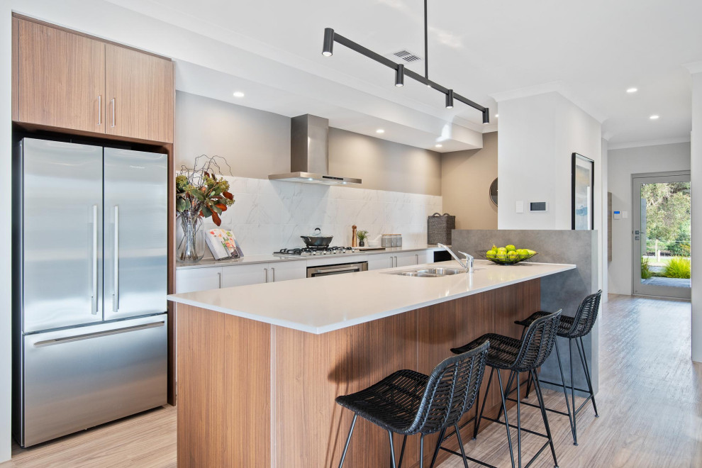This is an example of a contemporary galley kitchen in Perth with an undermount sink, flat-panel cabinets, white cabinets, white splashback, stainless steel appliances, medium hardwood floors, with island, brown floor and white benchtop.