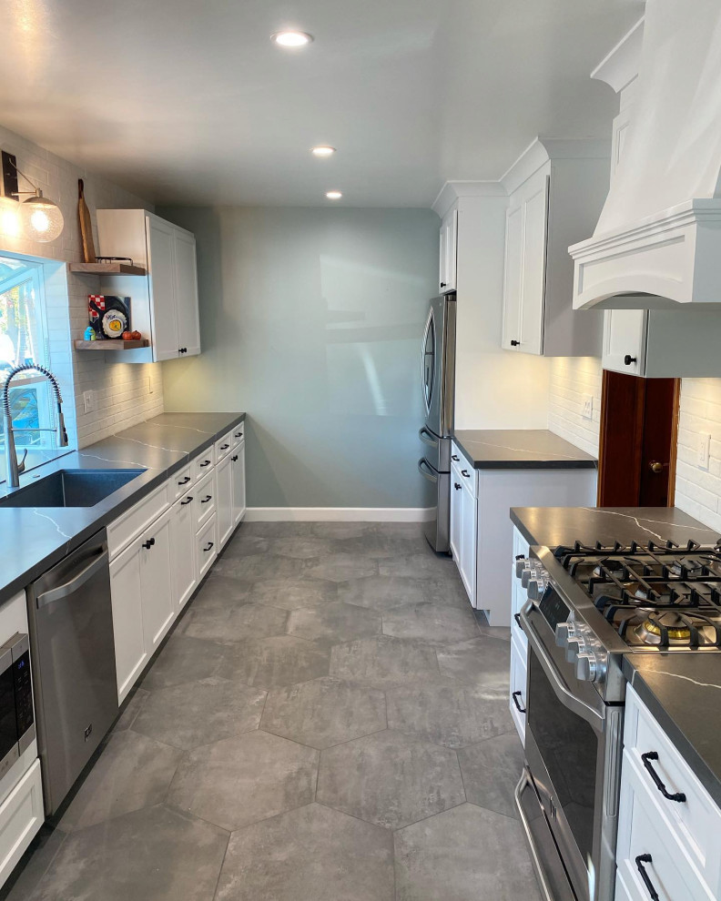 Mid-sized 1950s galley porcelain tile and gray floor kitchen photo in Orange County with a drop-in sink, shaker cabinets, white cabinets, quartz countertops, white backsplash, subway tile backsplash, stainless steel appliances, no island and black countertops