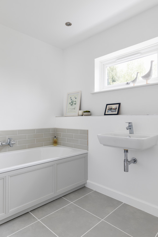 Design ideas for a mid-sized transitional kids bathroom in Oxfordshire with a drop-in tub, a wall-mount toilet, gray tile, ceramic tile, white walls, ceramic floors, a wall-mount sink and grey floor.