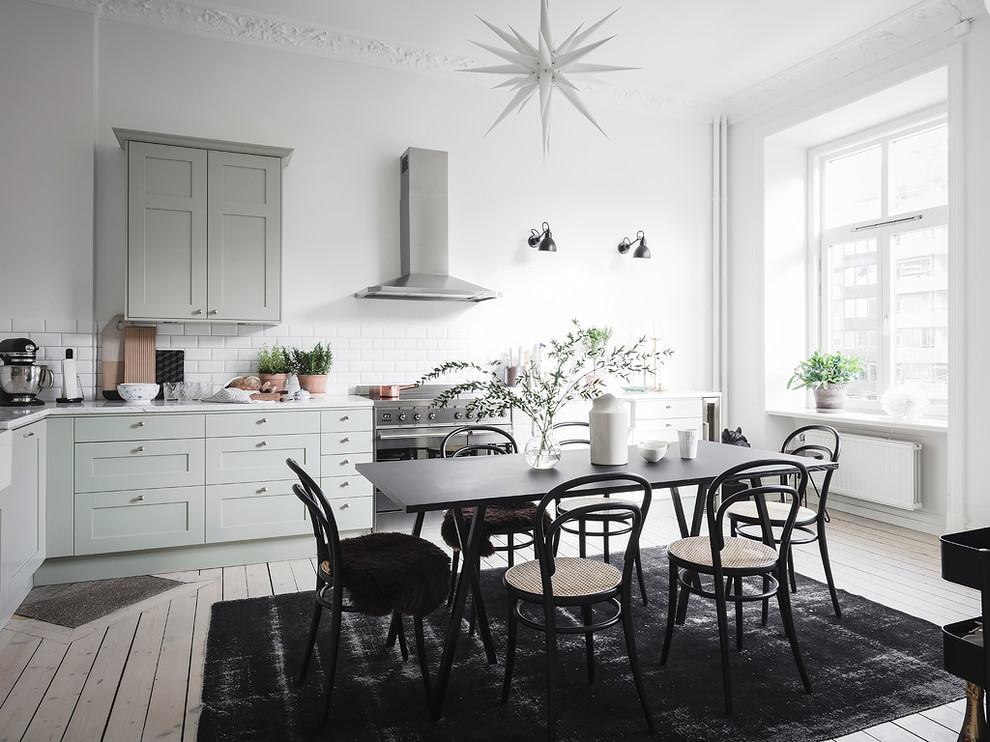 Scandinavian l-shaped eat-in kitchen in Gothenburg with shaker cabinets, green cabinets, white splashback, subway tile splashback, stainless steel appliances, painted wood floors, no island, white floor and white benchtop.