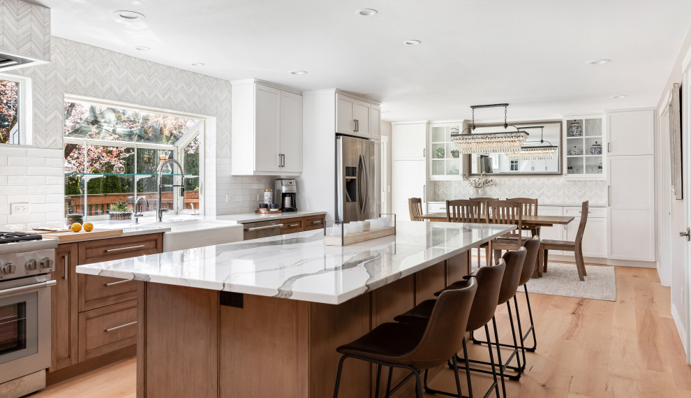 Example of a large transitional light wood floor and brown floor eat-in kitchen design in Seattle with a farmhouse sink, medium tone wood cabinets, quartz countertops, white backsplash, mosaic tile backsplash, stainless steel appliances, an island and white countertops