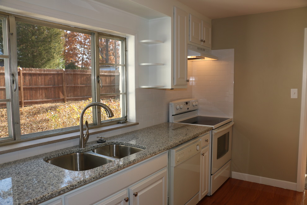 Example of a mid-sized classic l-shaped light wood floor eat-in kitchen design with an undermount sink, raised-panel cabinets, white cabinets, granite countertops, white backsplash, ceramic backsplash and white appliances