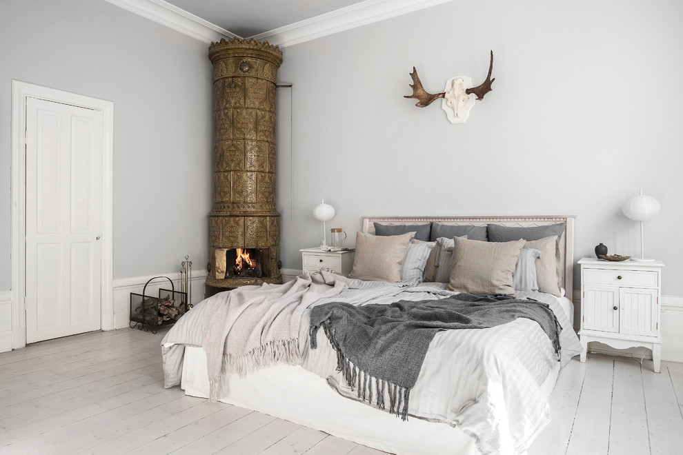 Mid-sized scandinavian master bedroom in Stockholm with painted wood floors, white floor, grey walls and a corner fireplace.