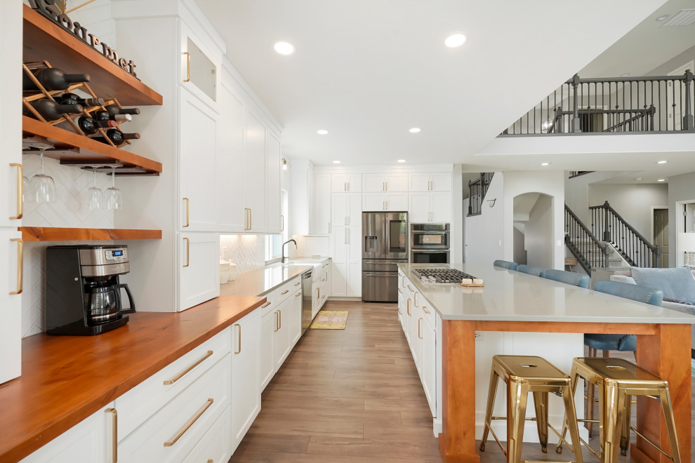 Open concept kitchen - large transitional l-shaped open concept kitchen idea in Denver with a farmhouse sink, shaker cabinets, white cabinets, quartz countertops, white backsplash, ceramic backsplash, stainless steel appliances, an island and gray countertops