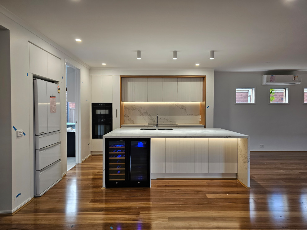 Photo of an open plan kitchen in Melbourne with a submerged sink, white cabinets, marble worktops, marble splashback, black appliances, light hardwood flooring and an island.