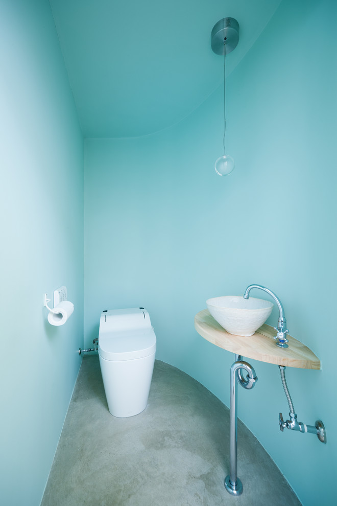 Scandinavian powder room with a one-piece toilet, blue walls, concrete floors, a vessel sink, wood benchtops and grey floor.