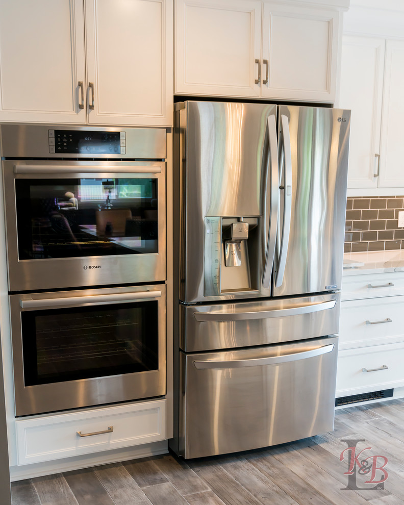 Mid-sized transitional porcelain tile and brown floor eat-in kitchen photo with an undermount sink, recessed-panel cabinets, white cabinets, quartz countertops, gray backsplash, subway tile backsplash, stainless steel appliances, an island and white countertops