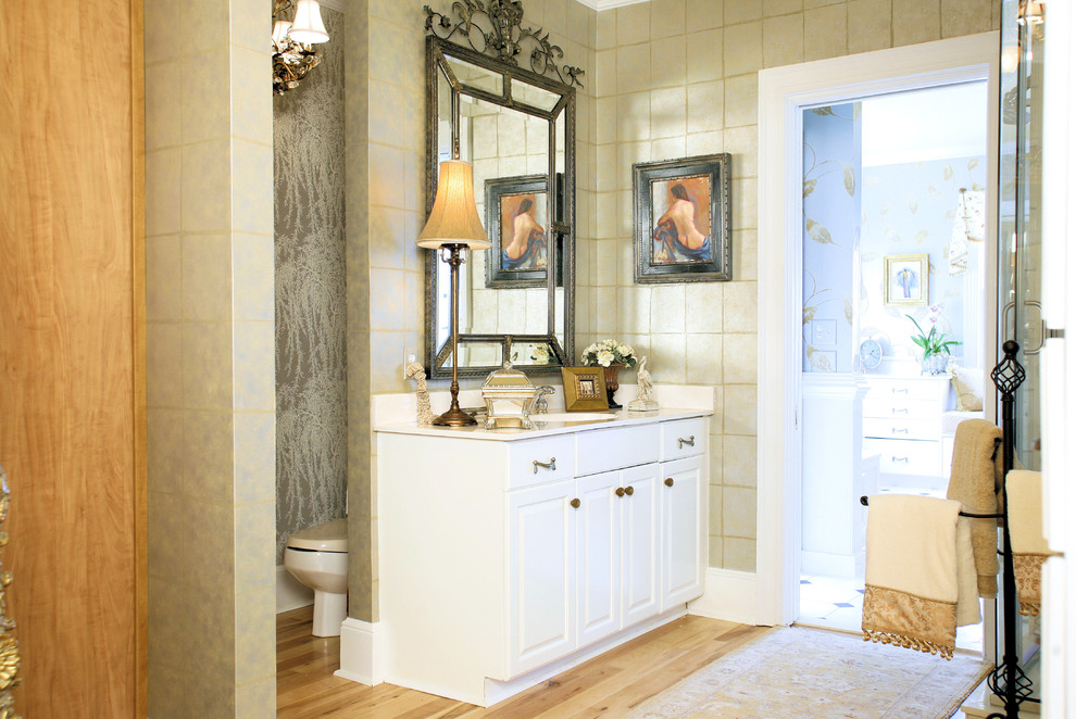 This is an example of a mid-sized transitional master bathroom in Charleston with an integrated sink, raised-panel cabinets, white cabinets, marble benchtops, a corner tub, a corner shower, a two-piece toilet, beige tile and light hardwood floors.