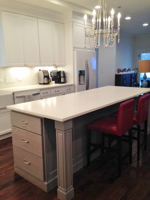 Example of a mid-sized transitional l-shaped dark wood floor eat-in kitchen design in Chicago with a farmhouse sink, recessed-panel cabinets, white cabinets, quartz countertops, white backsplash, ceramic backsplash, stainless steel appliances and an island