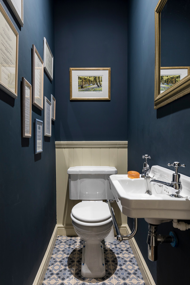 Photo of a small country powder room in London with a two-piece toilet, blue walls, porcelain floors, a wall-mount sink and blue floor.