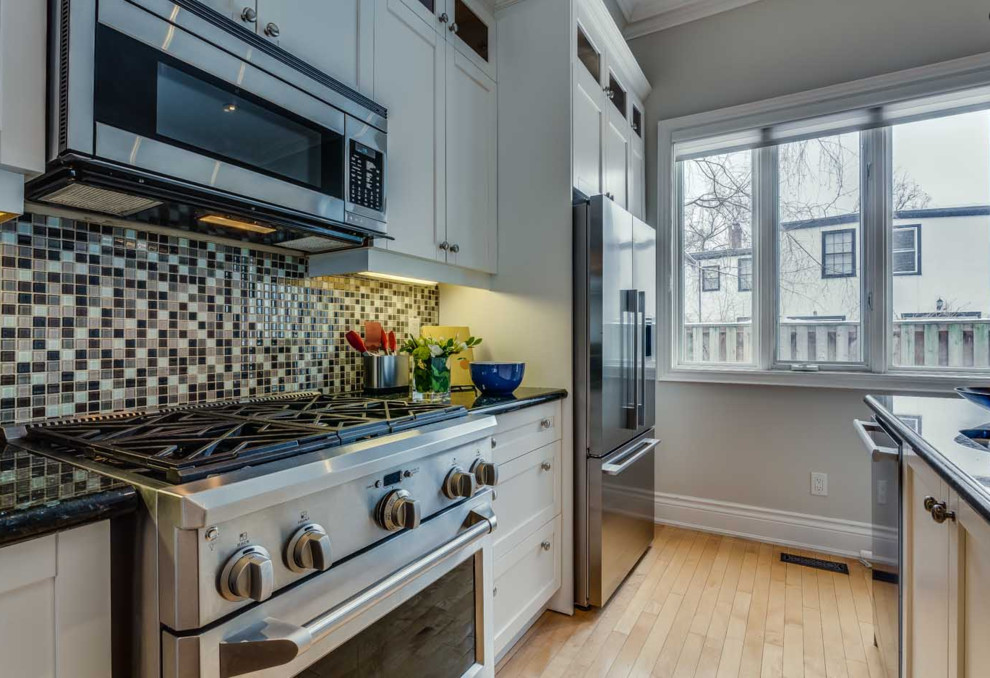 Example of a mid-sized transitional single-wall light wood floor and beige floor eat-in kitchen design in Toronto with a double-bowl sink, shaker cabinets, white cabinets, granite countertops, multicolored backsplash, mosaic tile backsplash, stainless steel appliances and an island