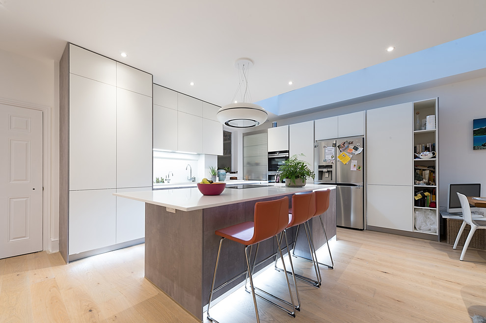 Photo of a mid-sized modern l-shaped kitchen in Hertfordshire with flat-panel cabinets, white cabinets, stainless steel appliances, light hardwood floors, with island and beige floor.