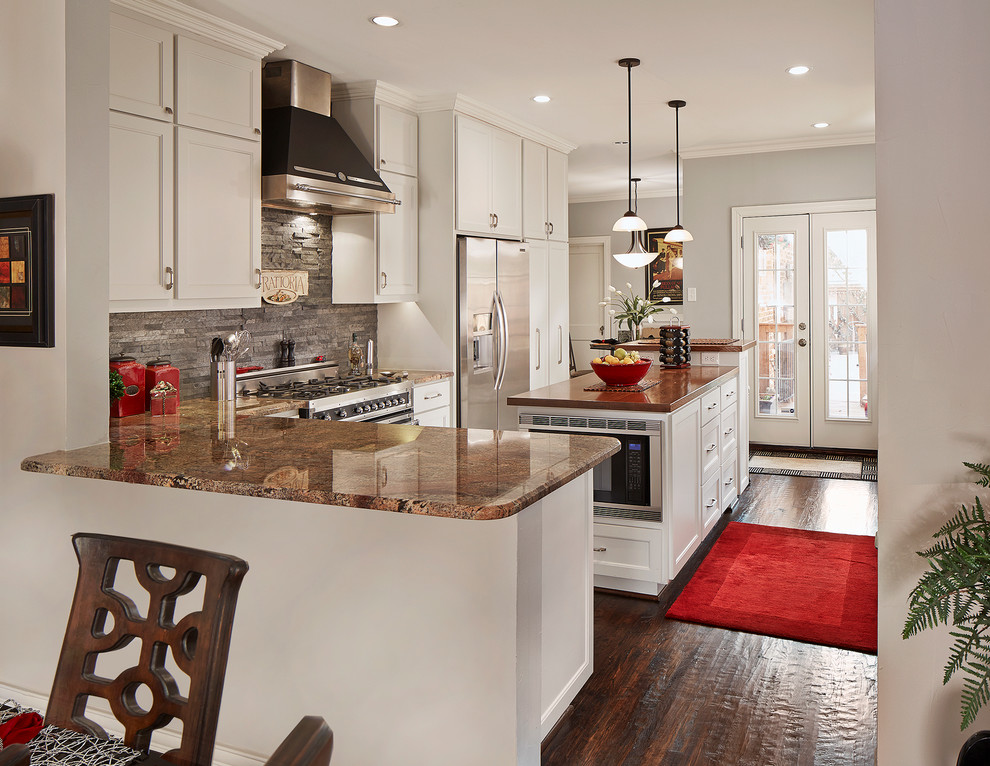 This is an example of a mid-sized traditional u-shaped kitchen in Dallas with recessed-panel cabinets, white cabinets, granite benchtops, grey splashback, slate splashback, black appliances, dark hardwood floors, with island and brown floor.
