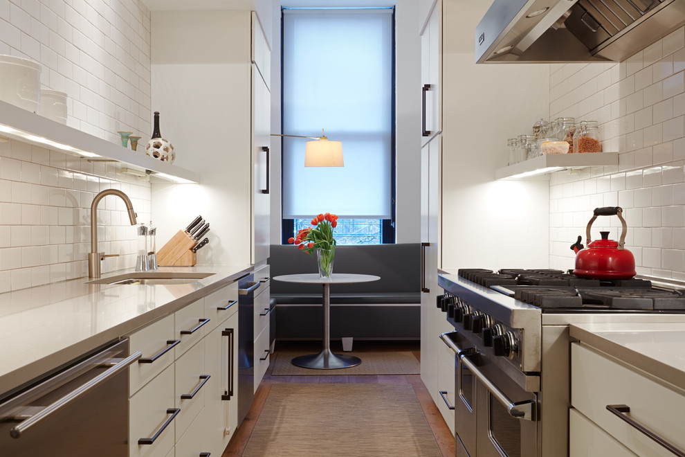 Inspiration for a large contemporary galley separate kitchen in New York with an undermount sink, flat-panel cabinets, white cabinets, white splashback, stainless steel appliances, medium hardwood floors, no island, brown floor, granite benchtops, ceramic splashback and grey benchtop.