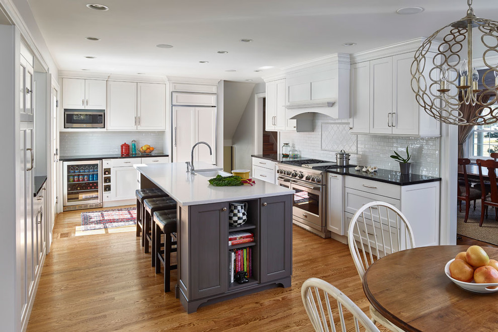 Photo of a mid-sized transitional eat-in kitchen in Philadelphia with recessed-panel cabinets, white cabinets, white splashback, ceramic splashback, medium hardwood floors and with island.