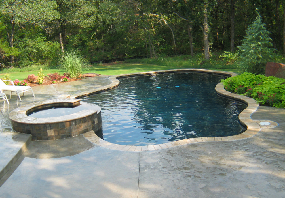Mid-sized beach style backyard custom-shaped natural pool in Oklahoma City with a hot tub and stamped concrete.